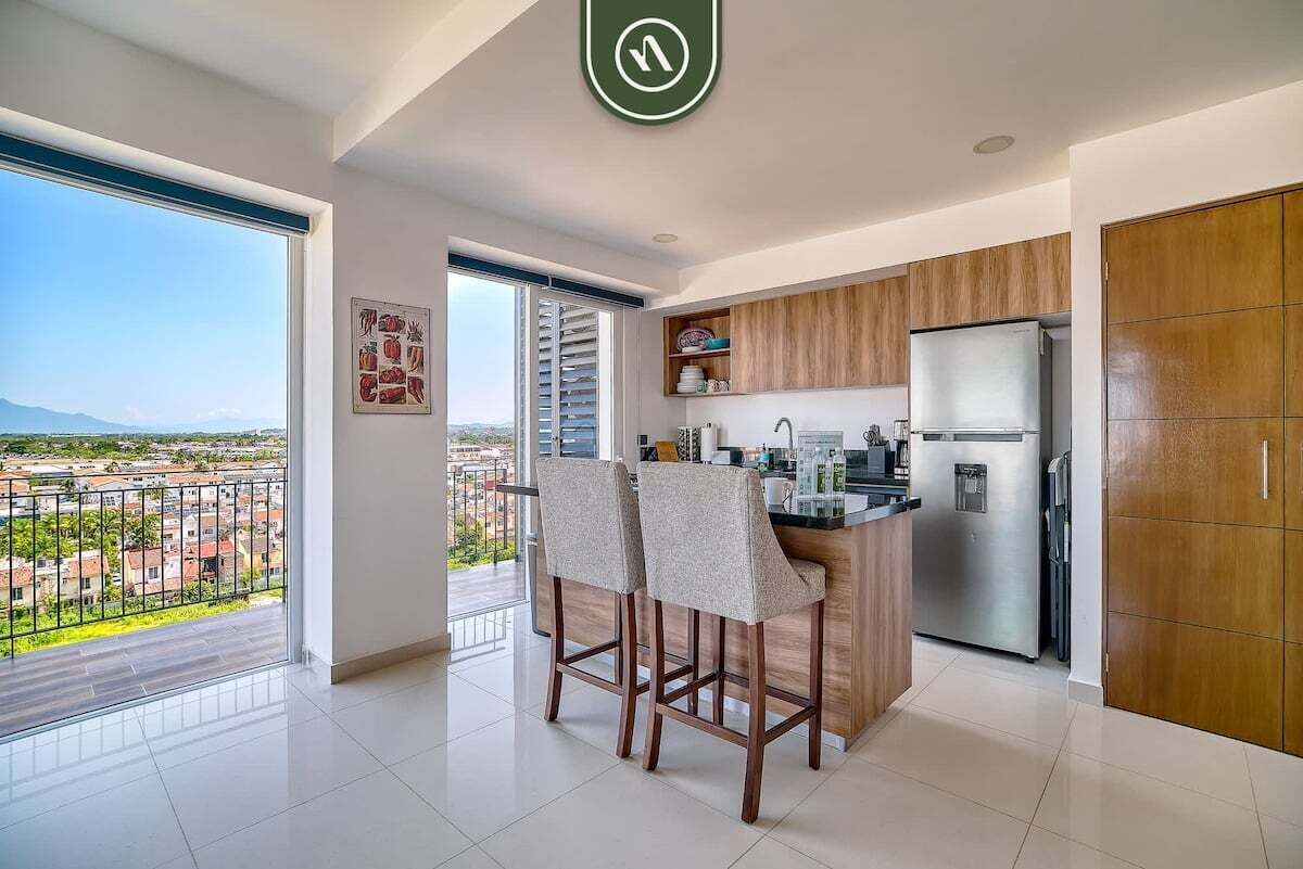 A modern kitchen with a large island, wooden cabinets, and a stainless steel refrigerator.