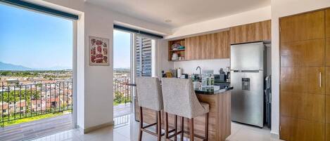 A modern kitchen with a large island, wooden cabinets, and a stainless steel refrigerator.