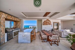 A modern kitchen with a stone wall, a large island, and a view of the ocean. - 2BR Condo With Rooftop Pool - 2 Min Walk to Beach (Bucerías)