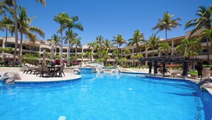 Ein Resort-Pool mit Palmen, Liegestühlen und einem Gebäude mit Balkonen.