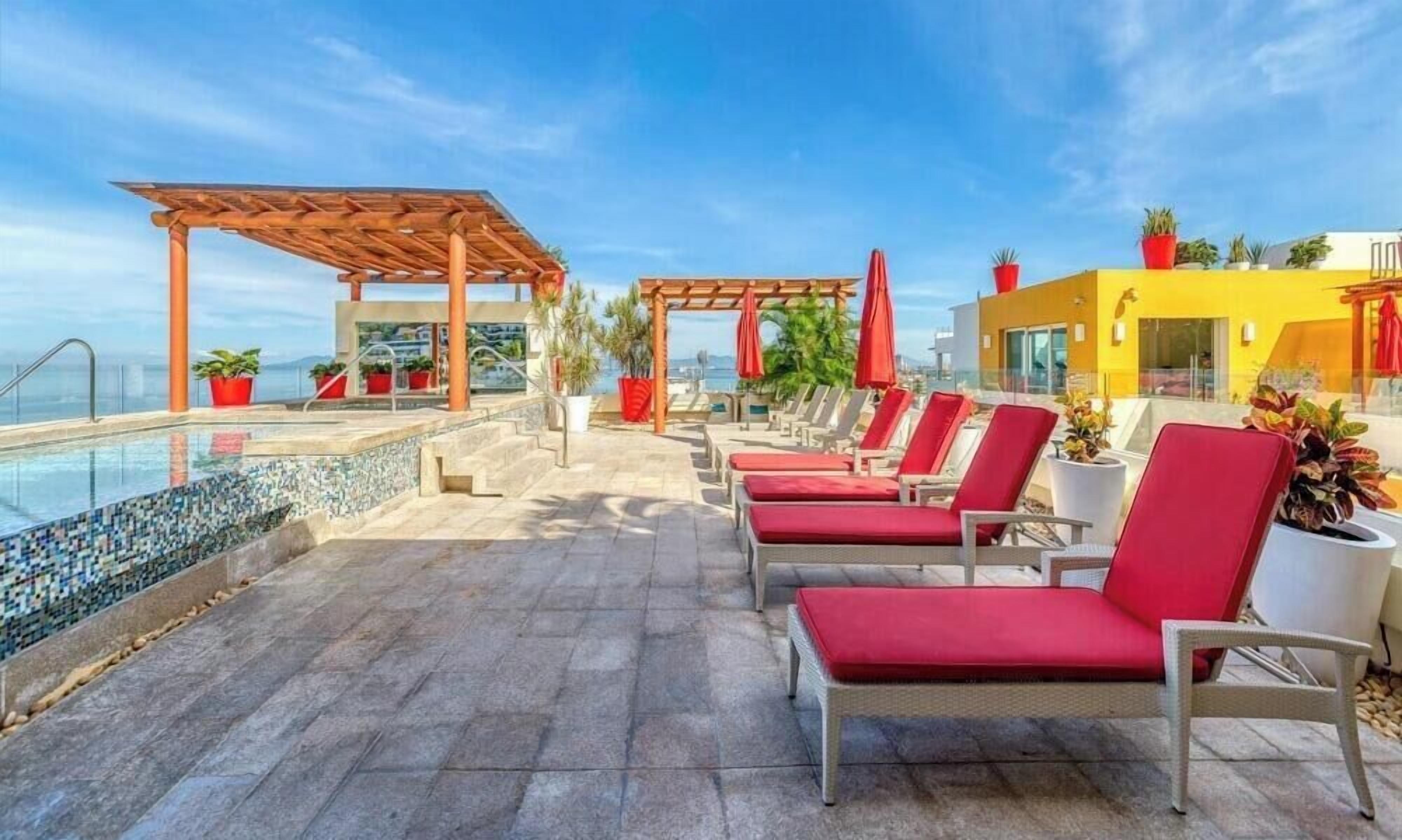 A rooftop pool area with lounge chairs, a pergola, and potted plants.