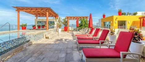 A rooftop pool area with lounge chairs, a pergola, and potted plants.