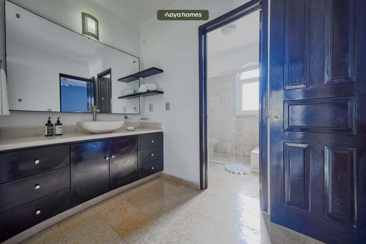 Un bany modern amb un mirall gran, un lavabo blanc i mobles de tocador fosc.