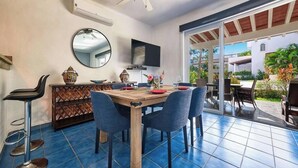 A dining area with a wooden table and chairs, a TV mounted on the wall, and a large mirror.