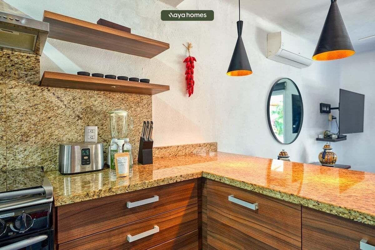 A modern kitchen with granite countertops, wooden cabinets, a built-in oven, and a hanging red chili pepper.