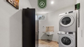 A laundry room with two stacked washing machines, a sink, and a door leading to another room. - Stunning 2 BR Condo - Oceanview Terrace - Downtown (Puerto Vallarta)