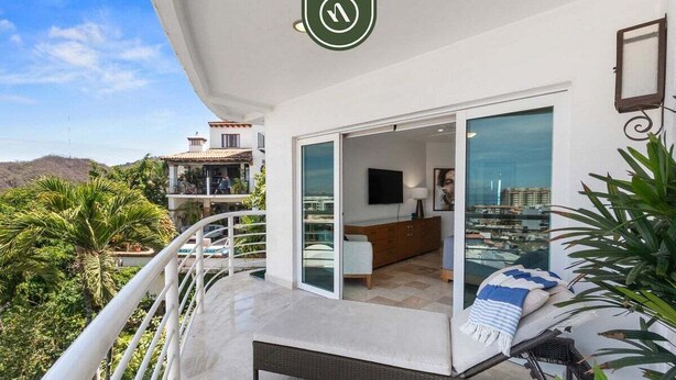 A balcony with a sofa, a TV, and a sliding glass door leading to an interior space. - Stunning 2 BR Condo - Oceanview Terrace - Downtown (Puerto Vallarta)