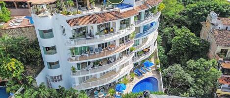 A multi-story hotel with balconies, a swimming pool, and lush greenery surrounding the property.