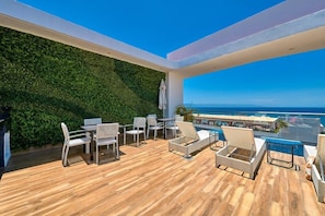 A balcony with a wooden floor, white furniture, and a green wall. - New 1 Br Unit 2 Min From Beach - Pool - King Bed (Puerto Vallarta)