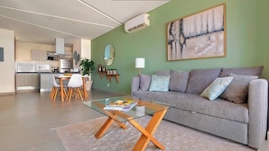 Una sala de estar moderna con una mesa de centro de vidrio, un sofá gris y una cocina al fondo.