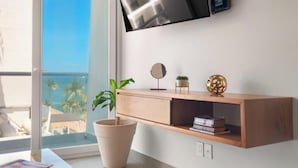 Una sala de estar moderna con un ventanal grande, una consola de madera, una planta en maceta, un espejo redondo y una esfera decorativa.