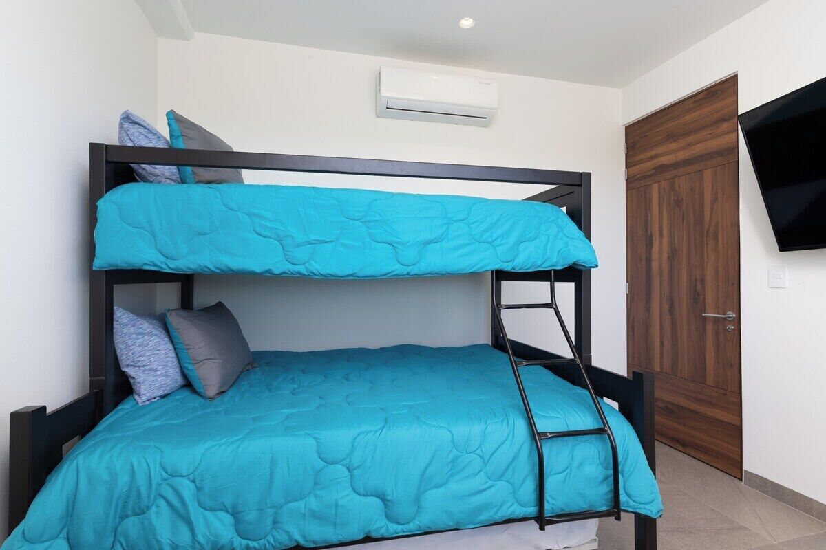 Un lit superposé avec une échelle, une armoire en bois et un téléviseur fixé au mur.