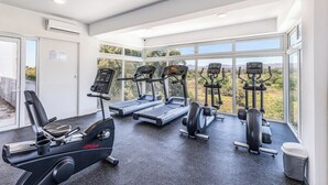 A gym with treadmills, an elliptical, and weight machines, featuring large windows and a view of the outdoors. - Believe Condo Flamingos Believe 302 (Bucerías)
