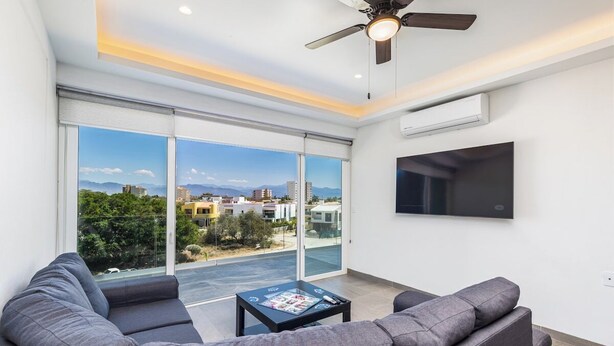 A modern living room with a large window, a ceiling fan, and a flat-screen TV. - Believe Condo Flamingos Believe 302 (Bucerías)
