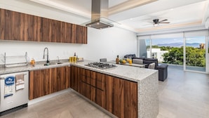 A modern kitchen with wooden cabinets, a granite countertop, and a built-in stove. - Believe Condo Flamingos Believe 302 (Bucerías)