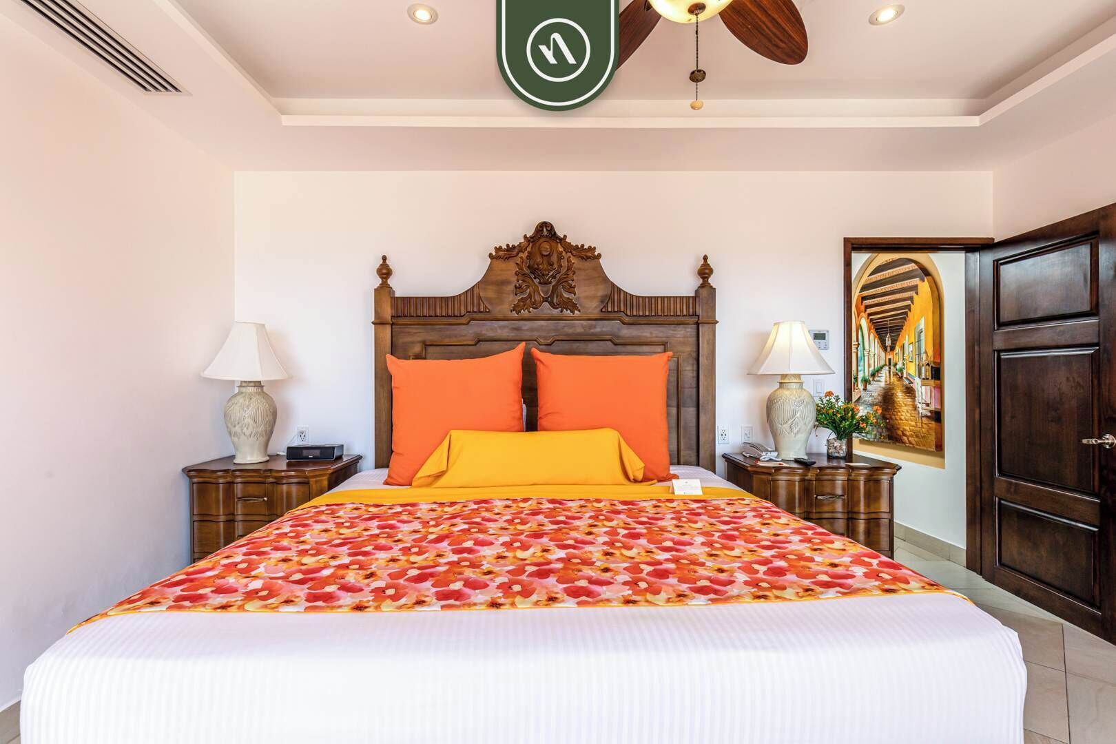 A hotel room with a large bed, two nightstands, a ceiling fan, and a decorative wall piece.