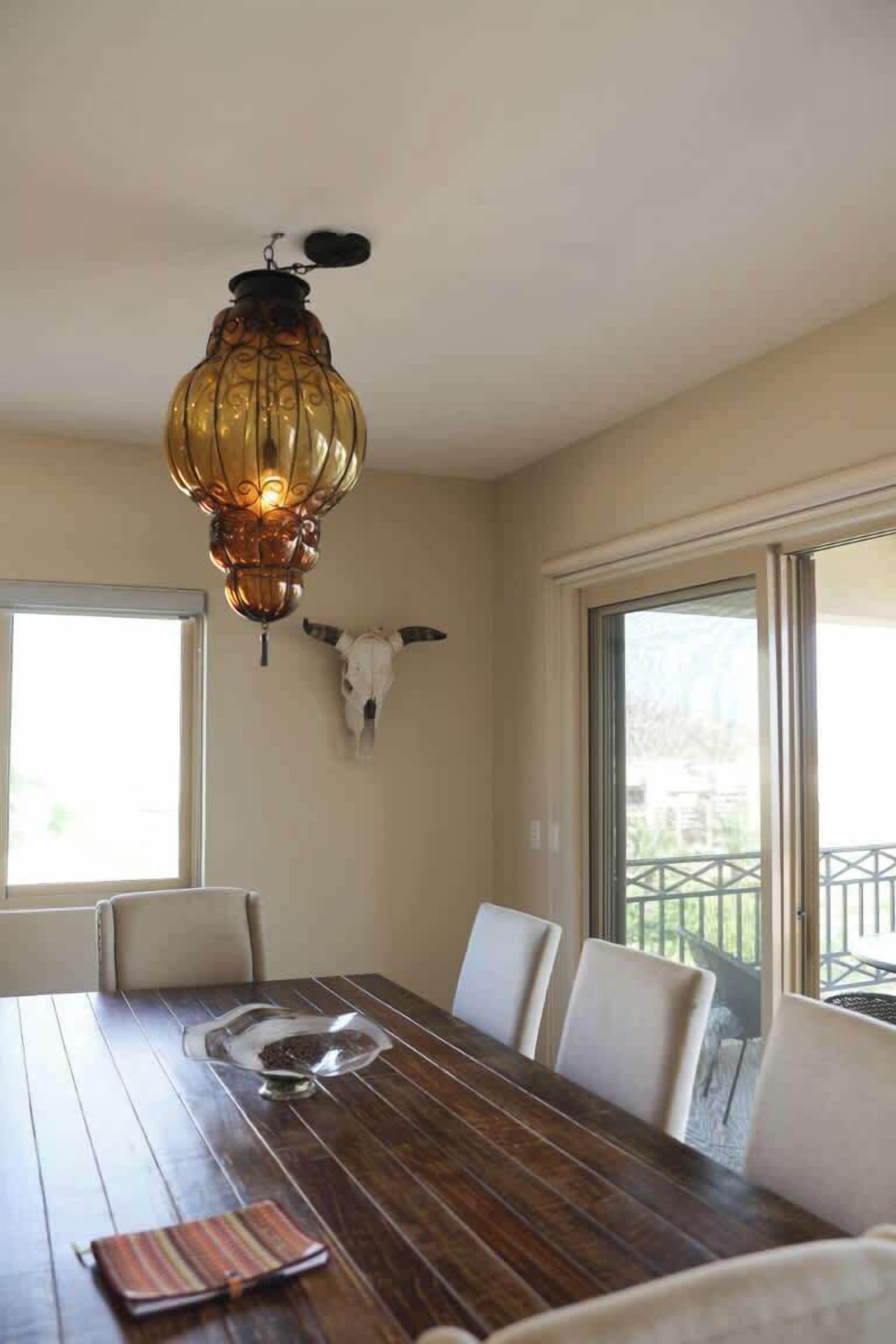 Un espace repas comprenant une table en bois, des chaises blanches, un saladier en verre et un luminaire décoratif.