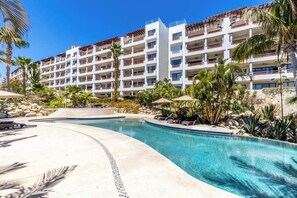 A resort with a swimming pool, palm trees, and a multi-story building with balconies. - New 2 BR Condo in San Jose - Pool - Tennis (San José del Cabo)
