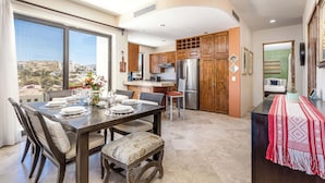 A modern kitchen with wooden cabinets, a stainless steel refrigerator, and a dining area with a table set for four. - New 2 BR Condo in San Jose - Pool - Tennis (San José del Cabo)