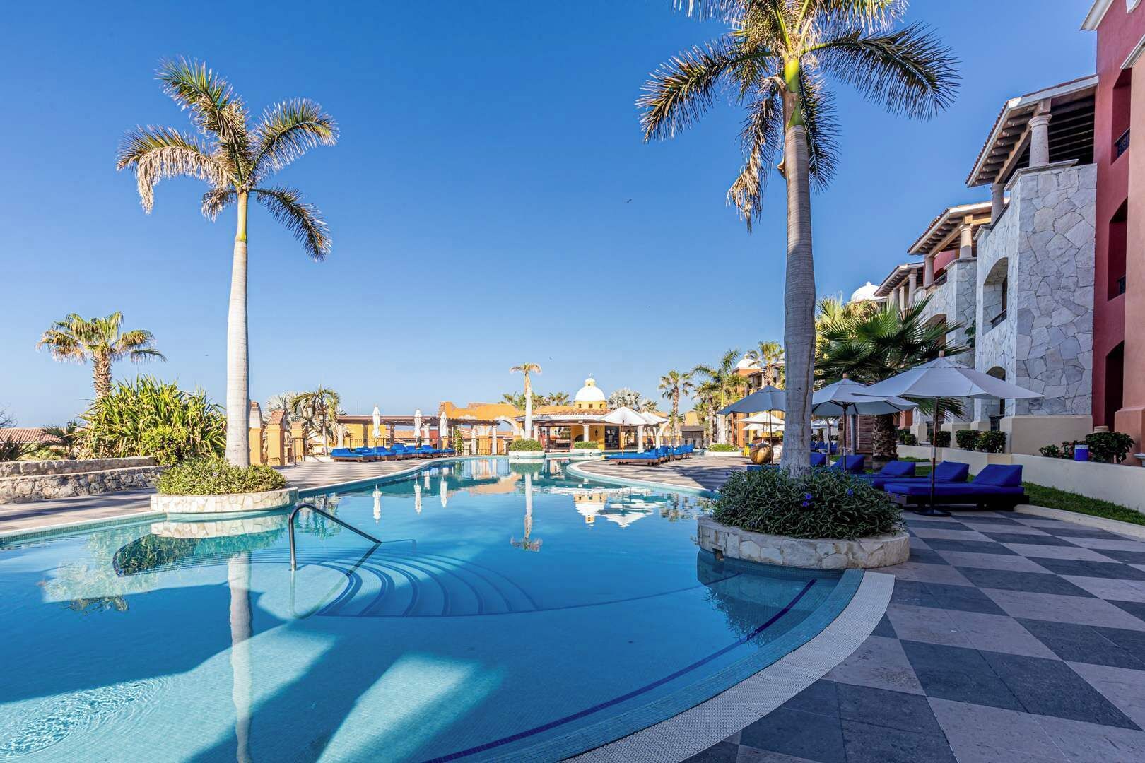 Ein Poolbereich eines Resorts mit Palmen, Liegestühlen und blauem Himmel.