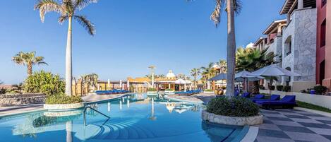 Ein Poolbereich eines Resorts mit Palmen, Liegestühlen und blauem Himmel.