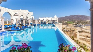 A pool with blue lounge chairs, white columns, and a view of the landscape. - Two Bdrm House With Ocean View in Cabo (Cabo San Lucas)