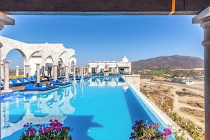 A pool with blue lounge chairs, white columns, and a view of the landscape.