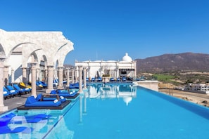 An infinity pool with blue lounge chairs, a white building with a dome, and a mountainous backdrop. - Two Bdrm House With Ocean View in Cabo (Cabo San Lucas)