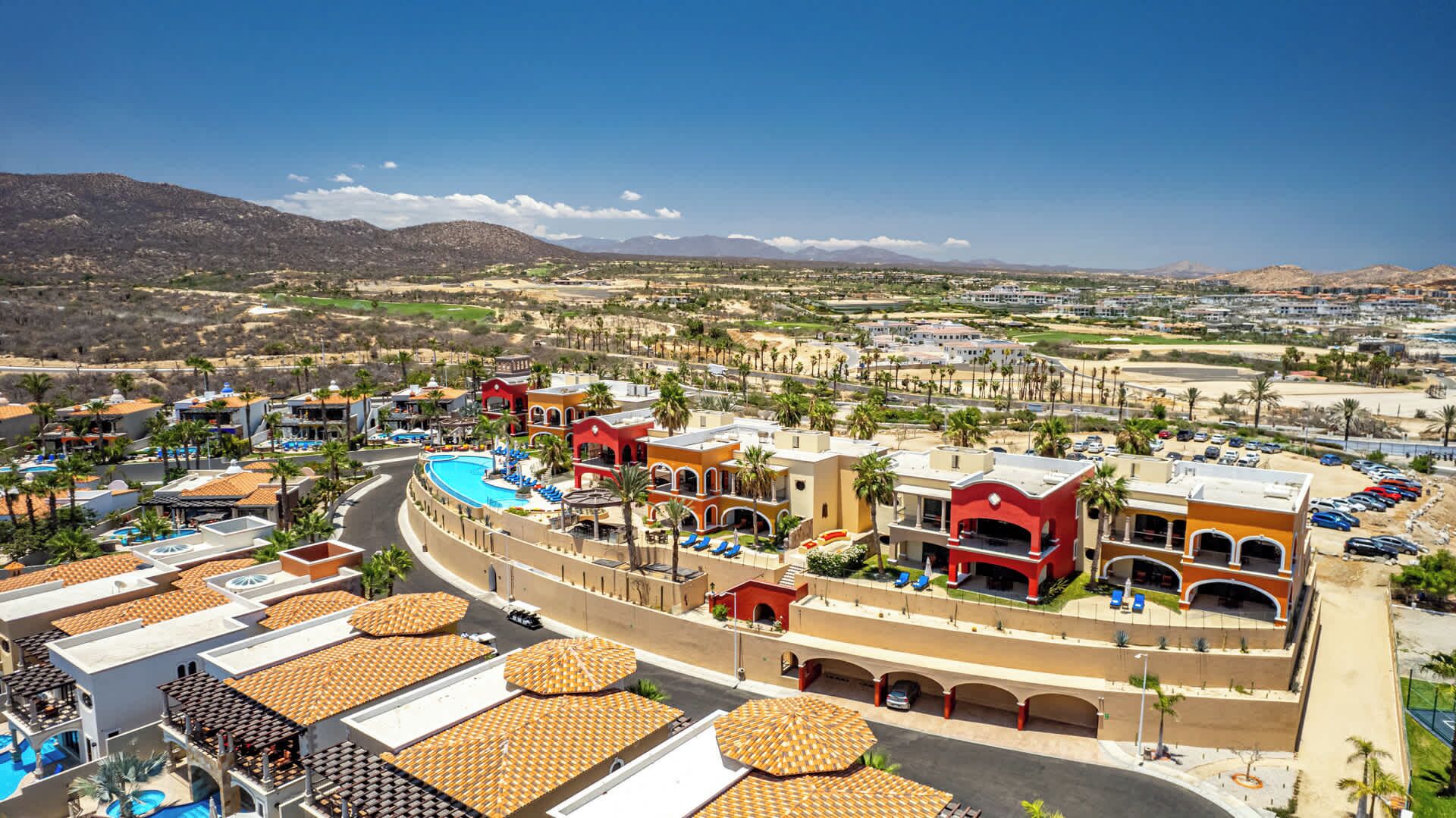 A resort with a swimming pool, multiple buildings, and a view of the surrounding landscape.