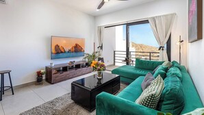 A modern living room with a green sofa, a flat-screen TV, and a ceiling fan. - Amazing 2BR Condo With Rooftop Pool - BBQ (Cabo San Lucas)