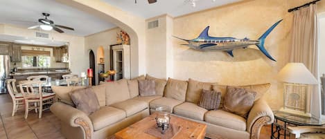 A living room with a beige sofa, a coffee table, and a dining area with chairs and a table.