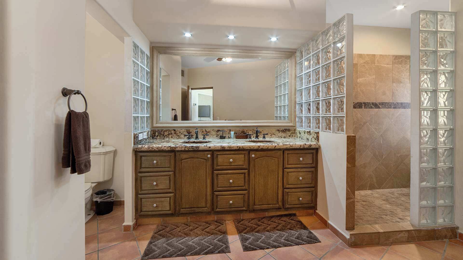 Un baño con un espejo grande, armarios de madera, encimera de mármol y cabina de ducha de vidrio.