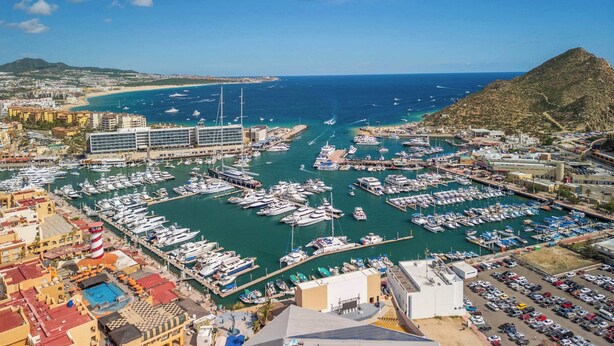A marina with numerous boats docked, a large hotel building, and a mountainous backdrop. - Amazing Studio - Terrace Overlooking the Marina (Cabo San Lucas)