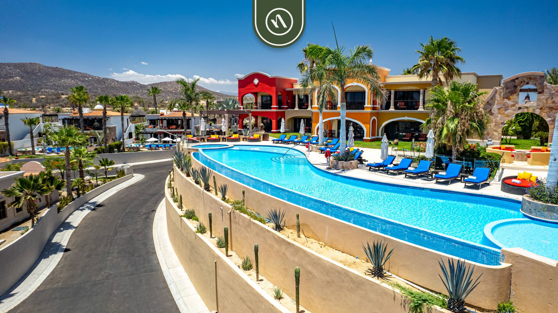 A resort with a large swimming pool, palm trees, and a mountain backdrop.