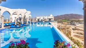 Una piscina con sillas reclinables azules y un edificio blanco con arcos al fondo.