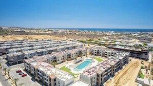 A residential complex with multiple apartment buildings, a swimming pool, and a view of the coastline. - Chic 2BR House - Pedregal - Private Rooftop - Pool (Cabo San Lucas)