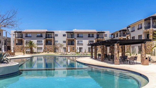 A swimming pool with lounge chairs, a covered seating area, and a building with balconies. - Chic 2BR House - Pedregal - Private Rooftop - Pool (Cabo San Lucas)