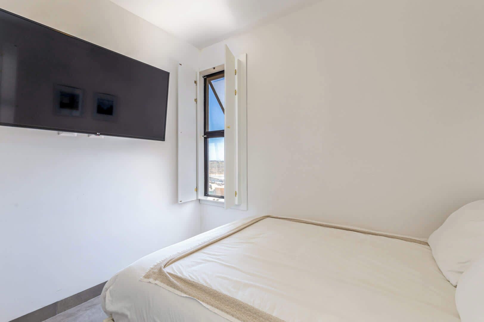 A bedroom with a bed, a window, and a wall-mounted TV.