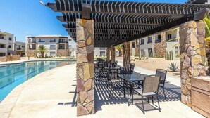 A poolside area with a pergola, stone pillars, and outdoor seating. - Chic 2BR House - Pedregal - Private Rooftop - Pool (Cabo San Lucas)