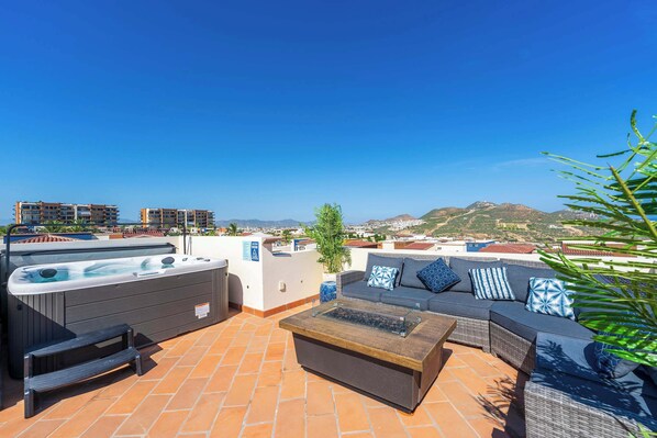 A rooftop terrace with a hot tub, seating area, and a view of the cityscape.
