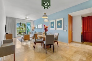 Une chambre d’hôtel avec un coin repas, une porte rouge et une vue sur des palmiers.