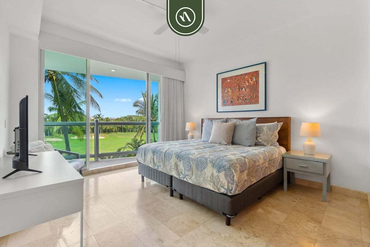 A modern bedroom with a large bed, a desk, and a balcony with a view of palm trees.