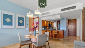 Ein modernes Wohnzimmer mit Esstisch, Stühlen und einer Küche im Hintergrund.