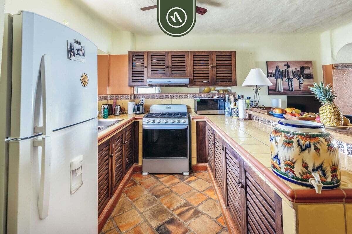 Une cuisine de taille réduite équipée d’un réfrigérateur, d’une cuisinière, d’un four à micro-ondes et de meubles de rangement en bois.