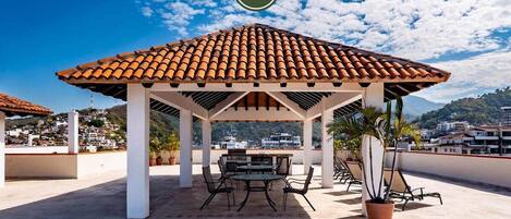 A rooftop patio with a tiled gazebo, a dining table, and chairs.