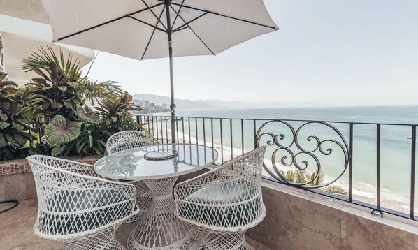 A balcony with a round table and chairs, an umbrella, and a view of the ocean.