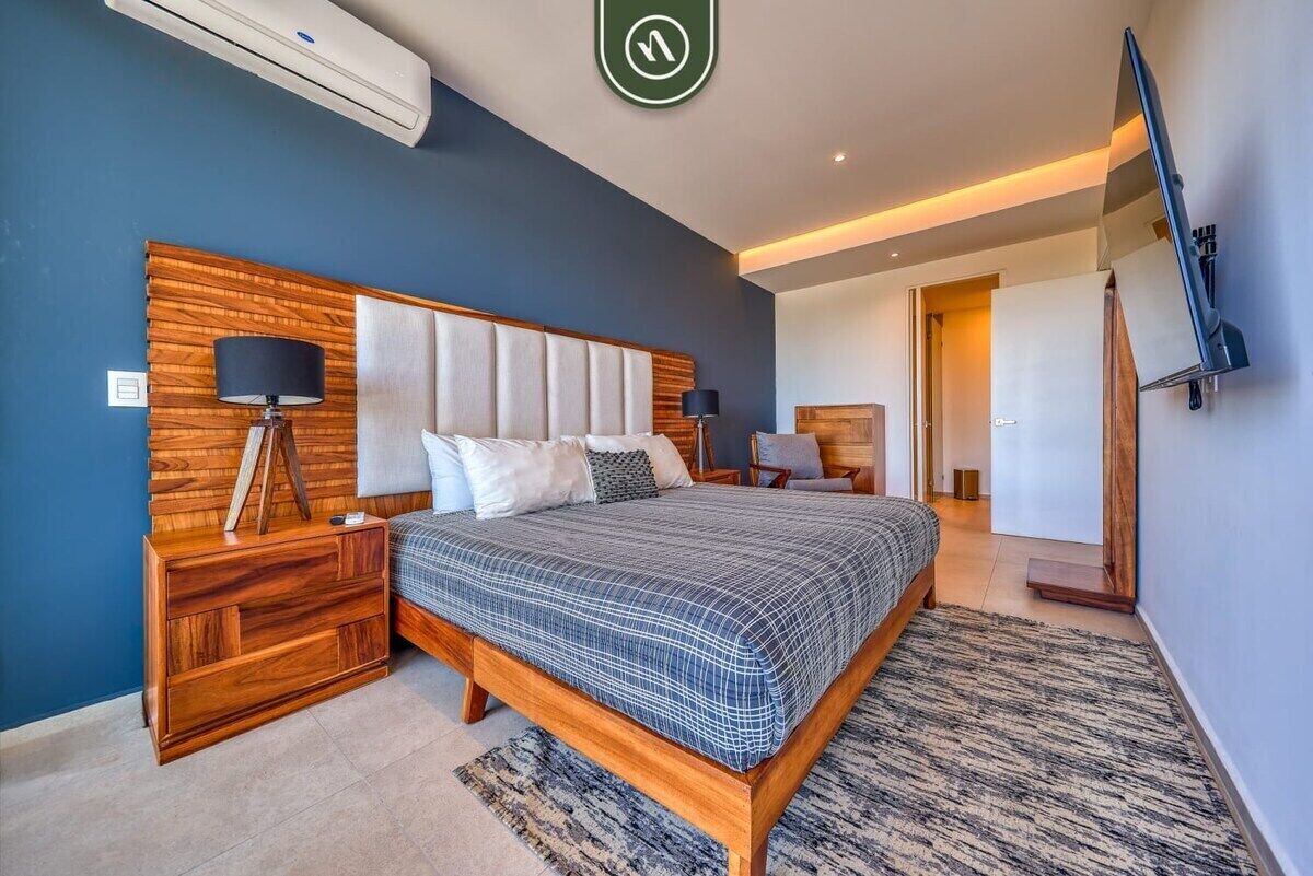 Un dormitorio moderno con una cama grande, cabecera de madera, mesitas de noche, un televisor de pantalla plana y un aire acondicionado de pared.