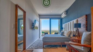 A modern bedroom with a large bed, a sofa, a TV, and a view of the outdoors. - Oceanfront 2BR Condo -private Balcony - Beach (Nuevo Nayarit)