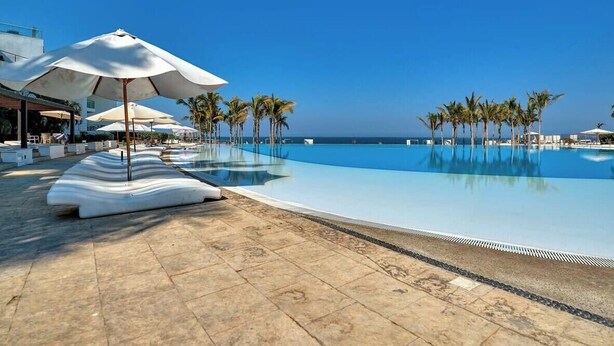 A swimming pool with lounge chairs and umbrellas, palm trees, and a clear sky. - Oceanfront 2BR Condo -private Balcony - Beach (Nuevo Nayarit)