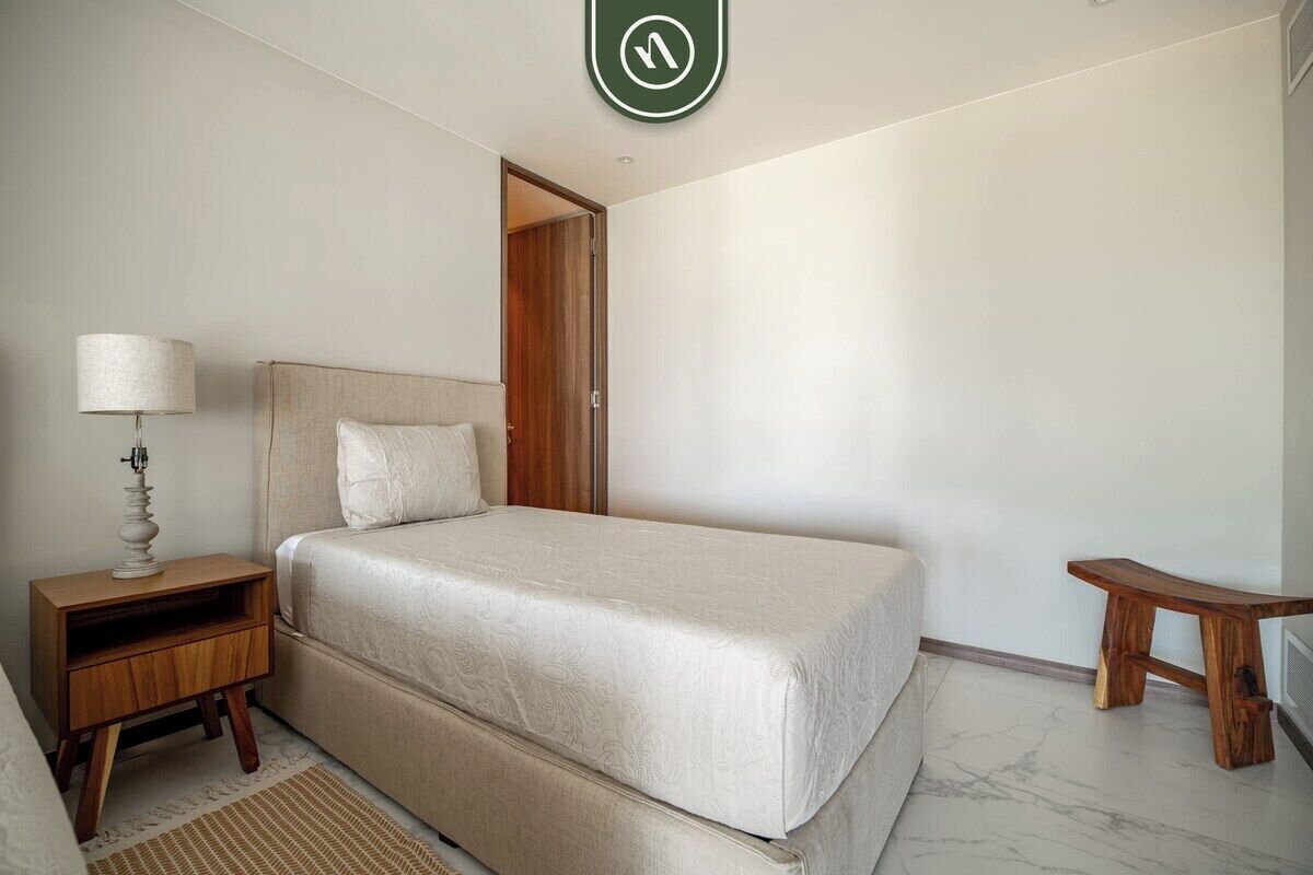 A bedroom with a bed, nightstand, lamp, and a small wooden stool.